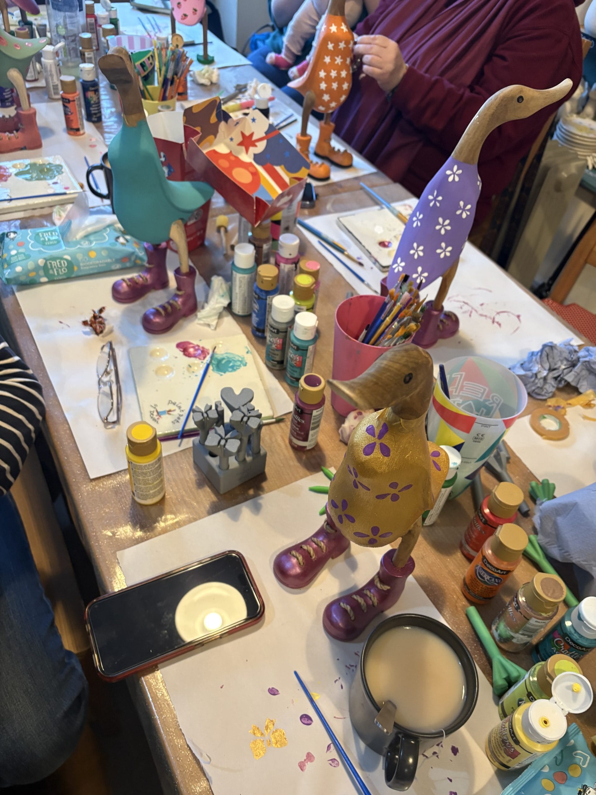 Colorful painted duck figurines in various designs on a craft table with art supplies.